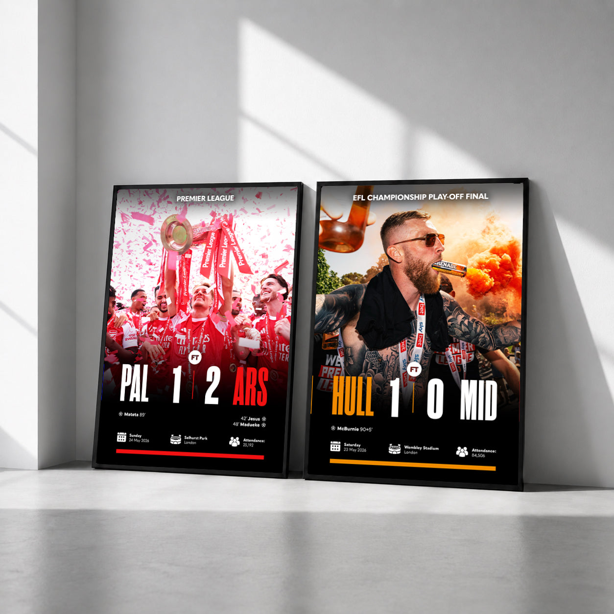 Two framed sports poster prints leaning against a light gray wall on a concrete floor, with dramatic diagonal sunlight casting shadows across the scene.