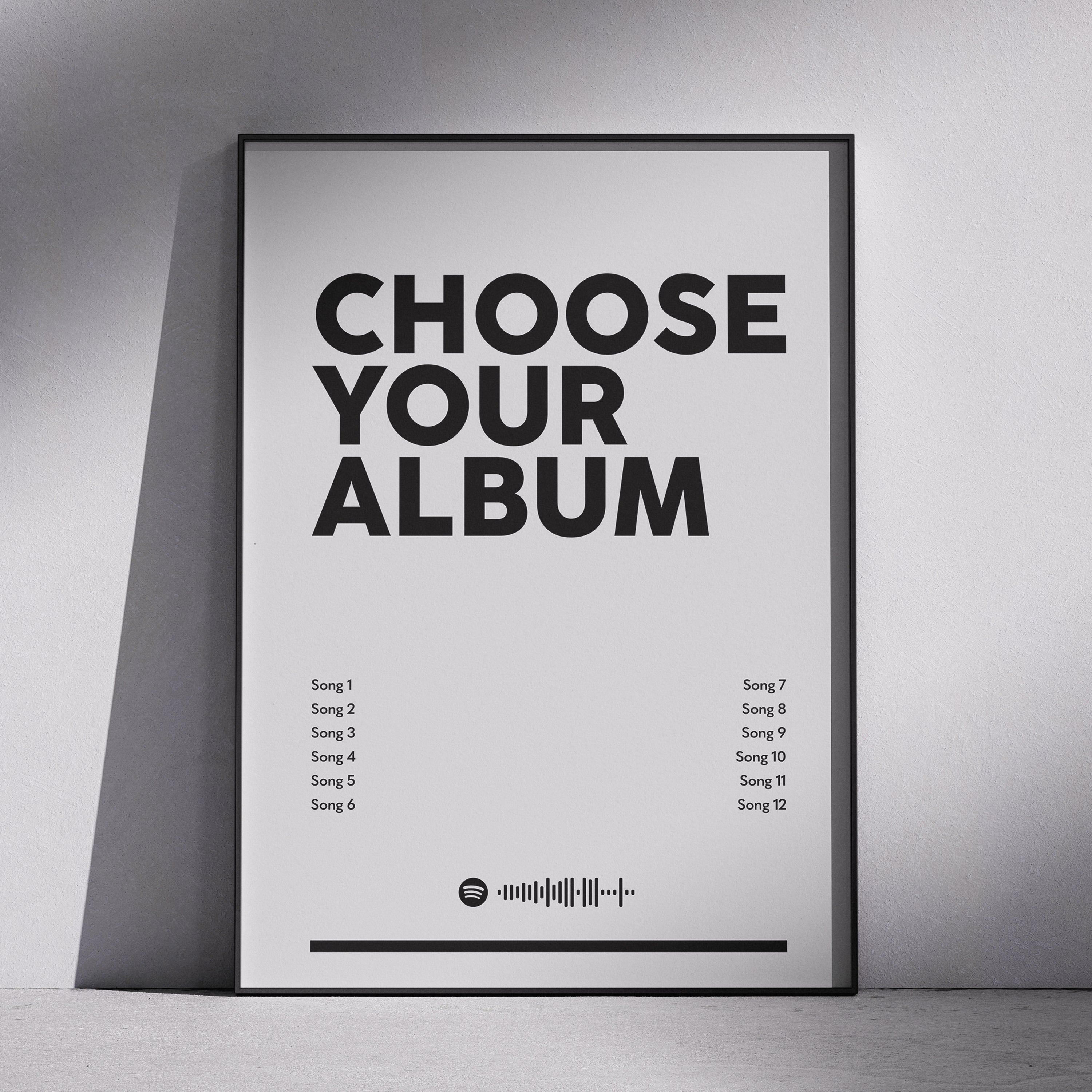 A framed minimalist poster leaning against a light gray wall on a floor, with large black text reading 'CHOOSE YOUR ALBUM' and small song titles arranged in two columns below.