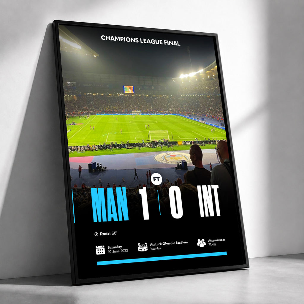 A framed vertical poster leaning against a white wall, showing a Champions League final match scene with a green stadium field, crowd, and large score text reading MAN 1 0 INT.