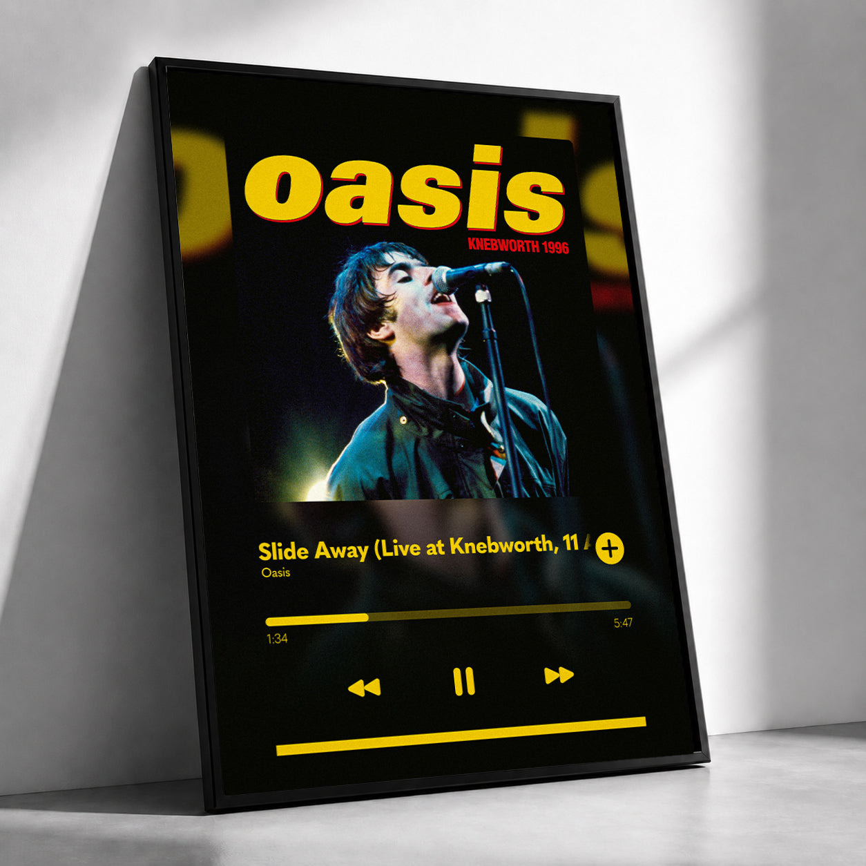 A framed Oasis 'Slide Away' music player-style poster leaning against a white wall on a light floor. The artwork shows the band name 'oasis' in large yellow letters above a photo of a performer at a microphone, with album text and playback controls on a black background.