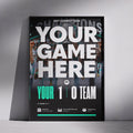 A framed sports event poster mockup leaning against a gray wall on a concrete floor. The poster features a black background with a blurred crowd photo, large white text reading 'YOUR GAME HERE', and teal accents including 'YOUR 1 0 TEAM'.