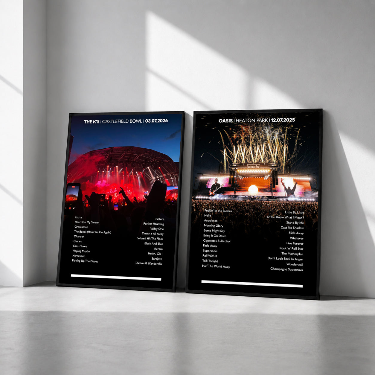 Two framed black concert poster prints leaning against a white wall in a minimalist room. The left print features a red-lit stadium scene for The K's Castlefield Bowl 2026, and the right print shows a stage scene for Oasis Heaton Park 2026, both with white event lineups printed below the images.